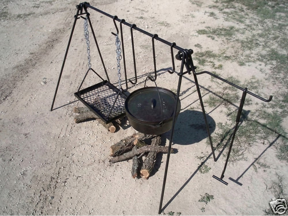 Portable quadpod campfire cooking system with hanging Dutch oven and adjustable grill grate over a wood fire.
