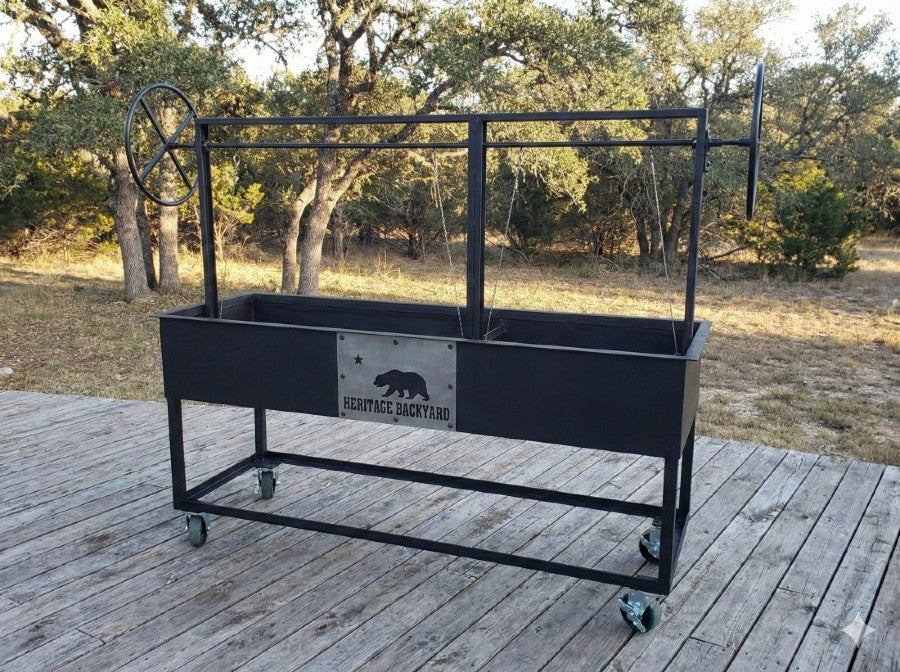 Split Santa Maria Style Grill by Heritage Backyard. Freestanding charcoal and wood grill with independent dual lift mechanisms, side wheels, and decorative bear emblem.