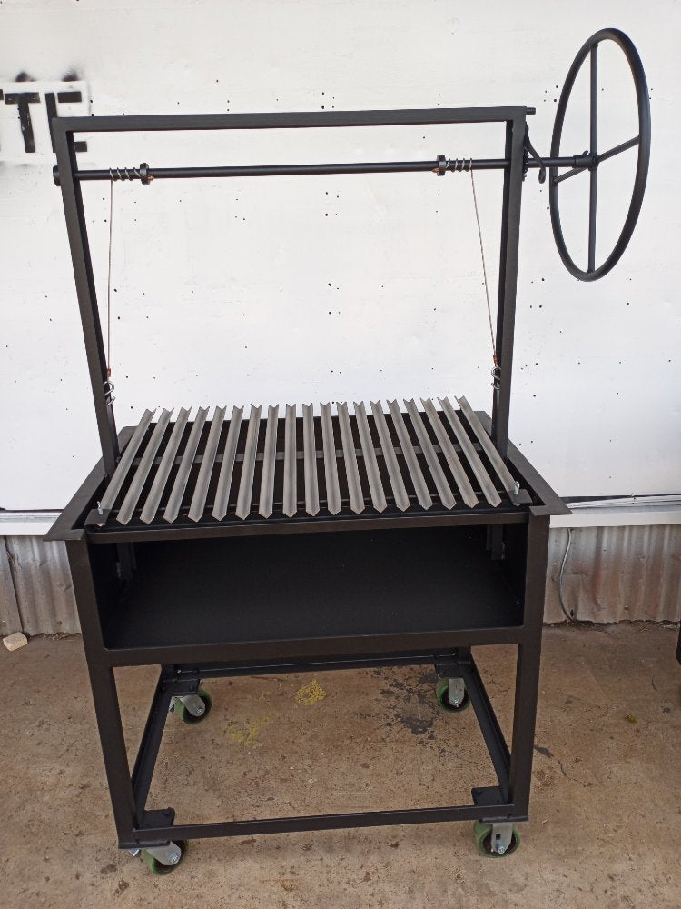 Argentine BBQ Grill with open firebox and stainless V-grate, mounted on a black steel frame with side wheel and heavy-duty casters.