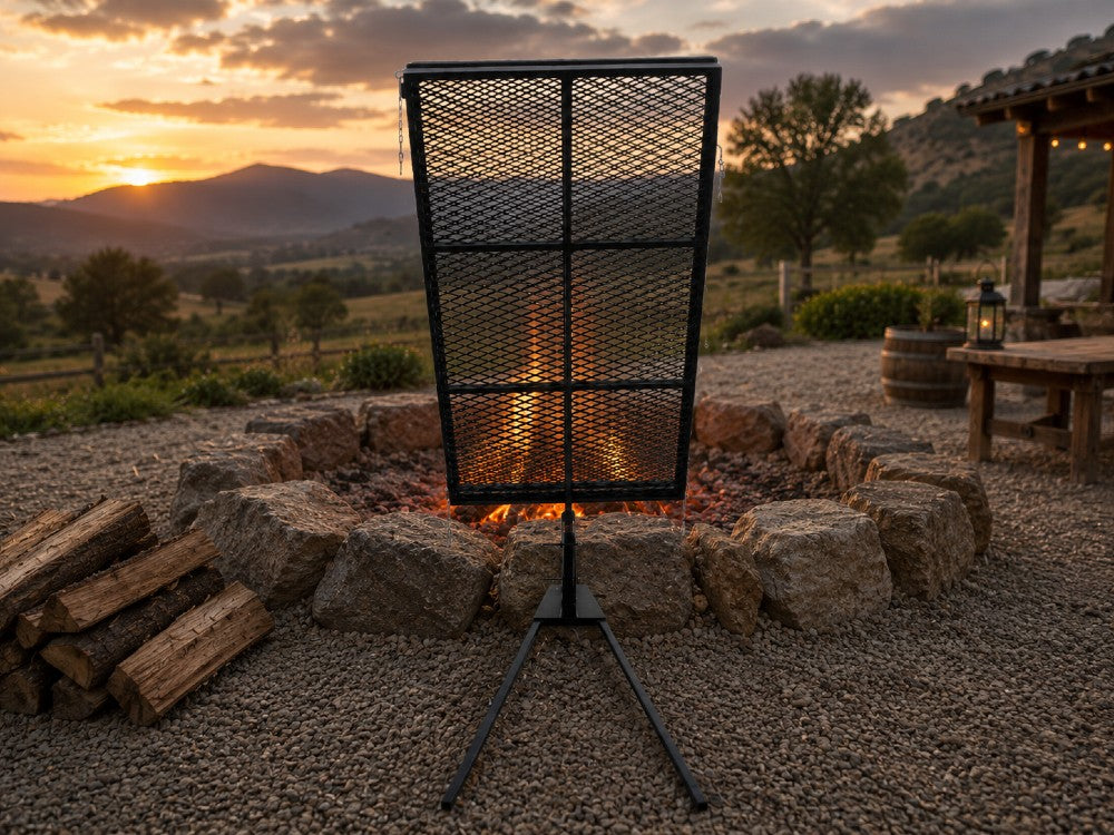 Asado Poultry Cross with Adjustable Base positioned beside a stone fire pit in a mountain ranch setting at sunset for authentic Argentine-style live fire cooking