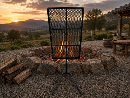 Asado Poultry Cross with Adjustable Base positioned beside a stone fire pit in a mountain ranch setting at sunset for authentic Argentine-style live fire cooking