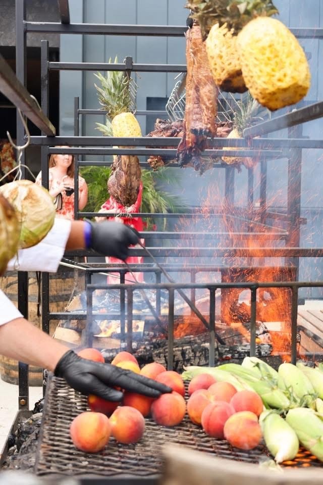 Chef grilling peaches and corn on Portico wood-fired BBQ grill with hanging pineapples