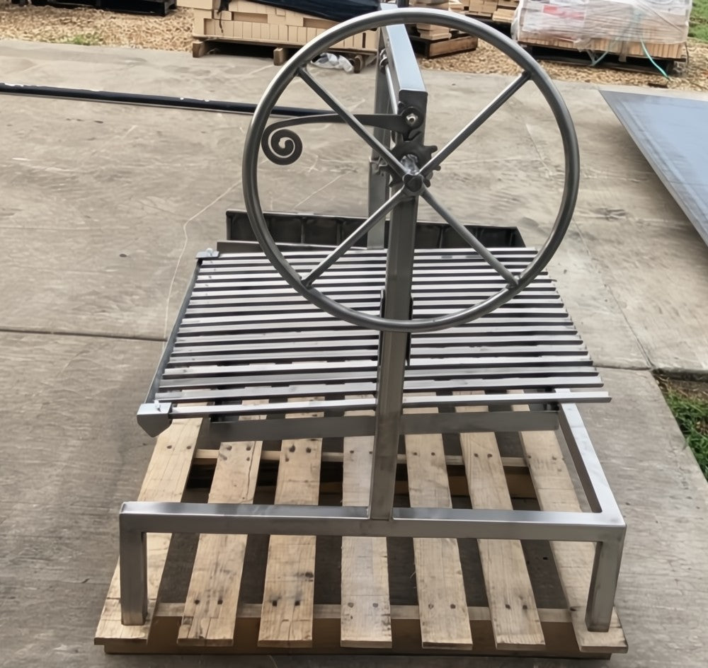 Side view of stainless steel adjustable stilt grill with side wheel height control and side brasero for wood or charcoal cooking