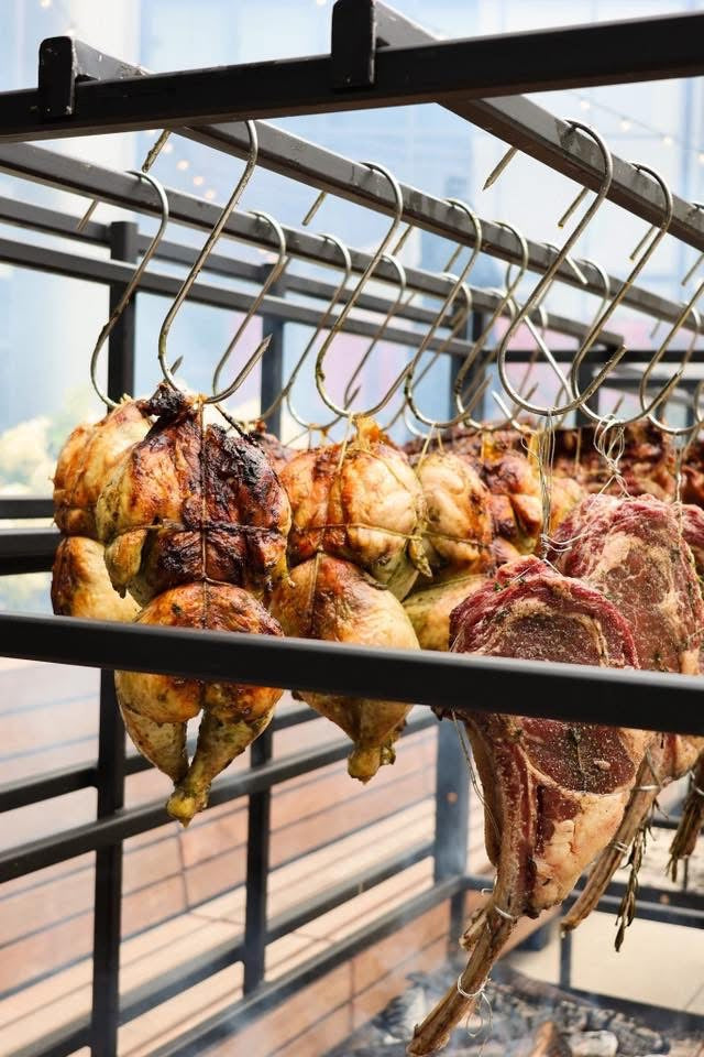 Whole chickens and tomahawk steaks cooking over live fire on Portico open-air grill